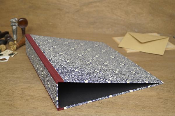 Folder lying flat, laminated with Carta Varese paper, matt blue with a creamy white pattern, geometric ornament white dove